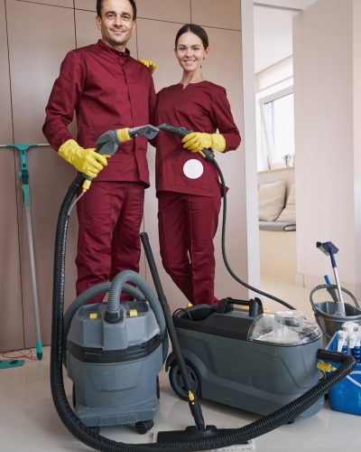Smiling young female cleaner and her pleased male colleague standing in room