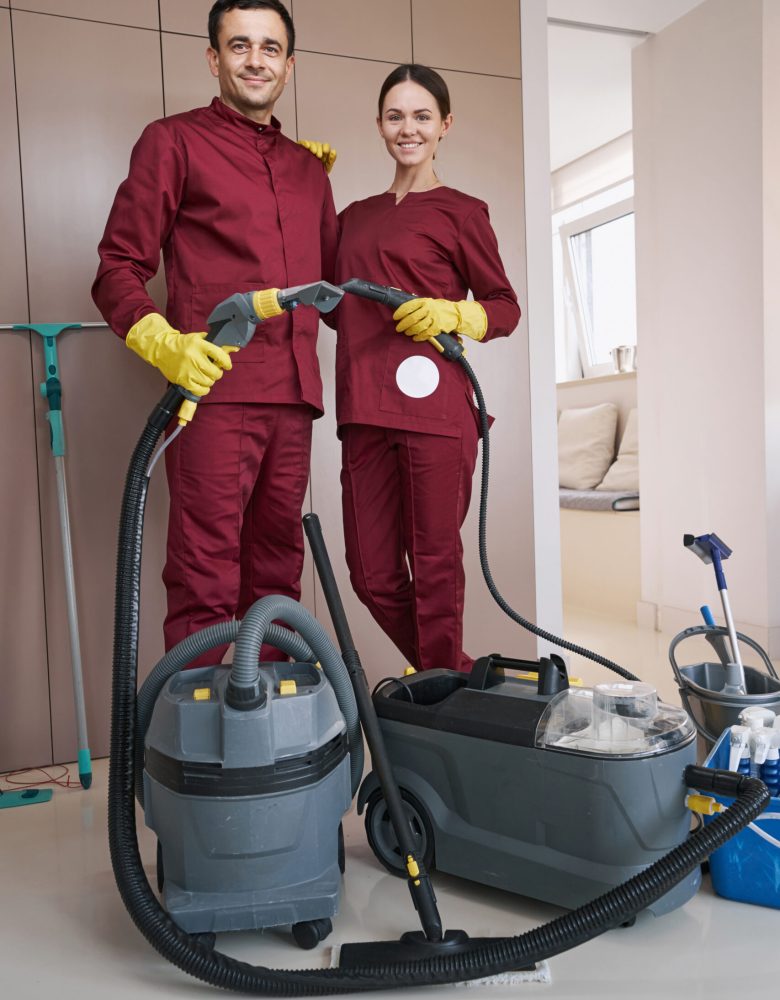 Smiling young female cleaner and her pleased male colleague standing in room
