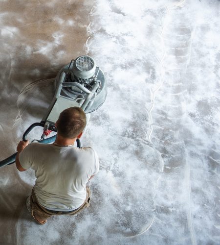 Construction worker in a family home living room that grind the concrete surface before applying epoxy flooring.Polyurethane and epoxy flooring.Concrete grinding.